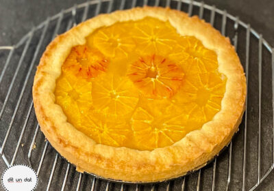 Ein runder Mürbeteigkuchen auf einem Kuchenrost, belegt mit Orangenscheiben.